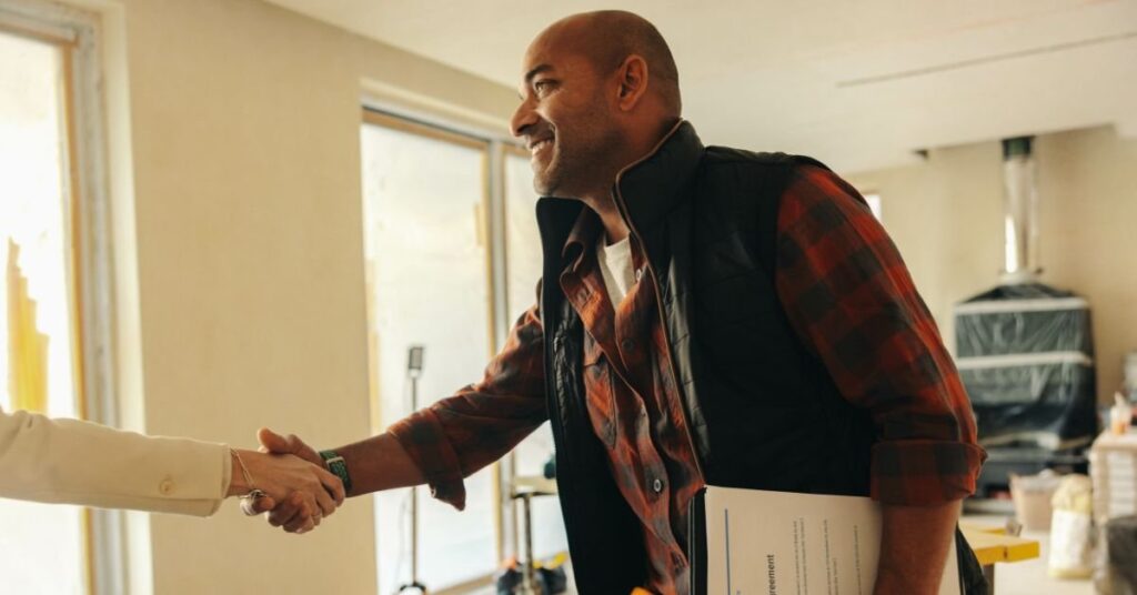 A man and woman shaking hands inside a cozy home, symbolizing agreement or partnership.